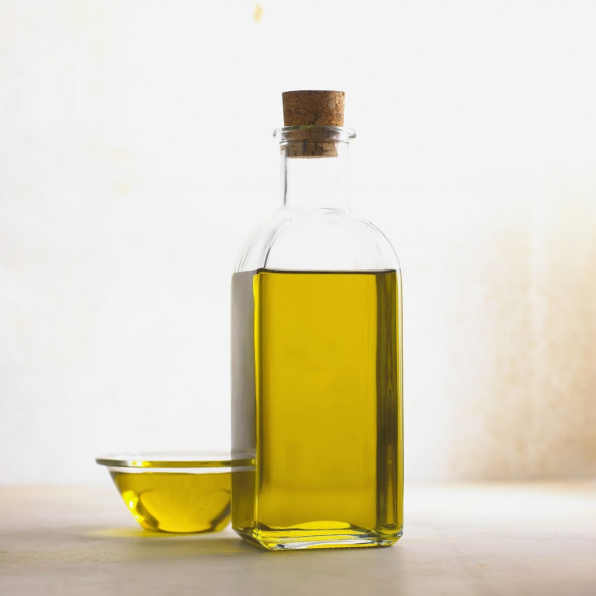Botella de vidrio con aceite dorado y tapón de corcho sobre fondo claro