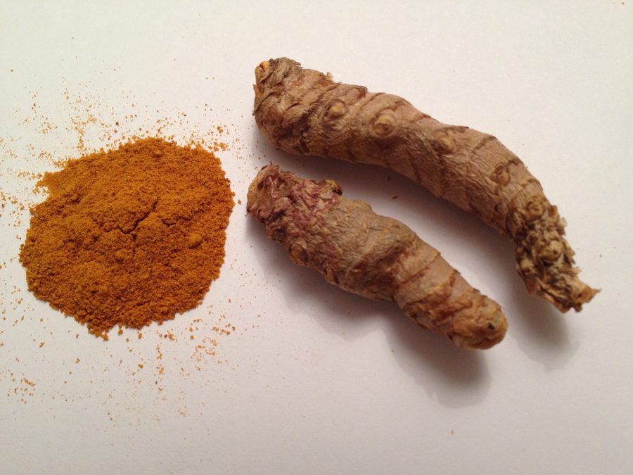 Cúrcuma fresca y limón cortado junto a una jarra de infusión dorada