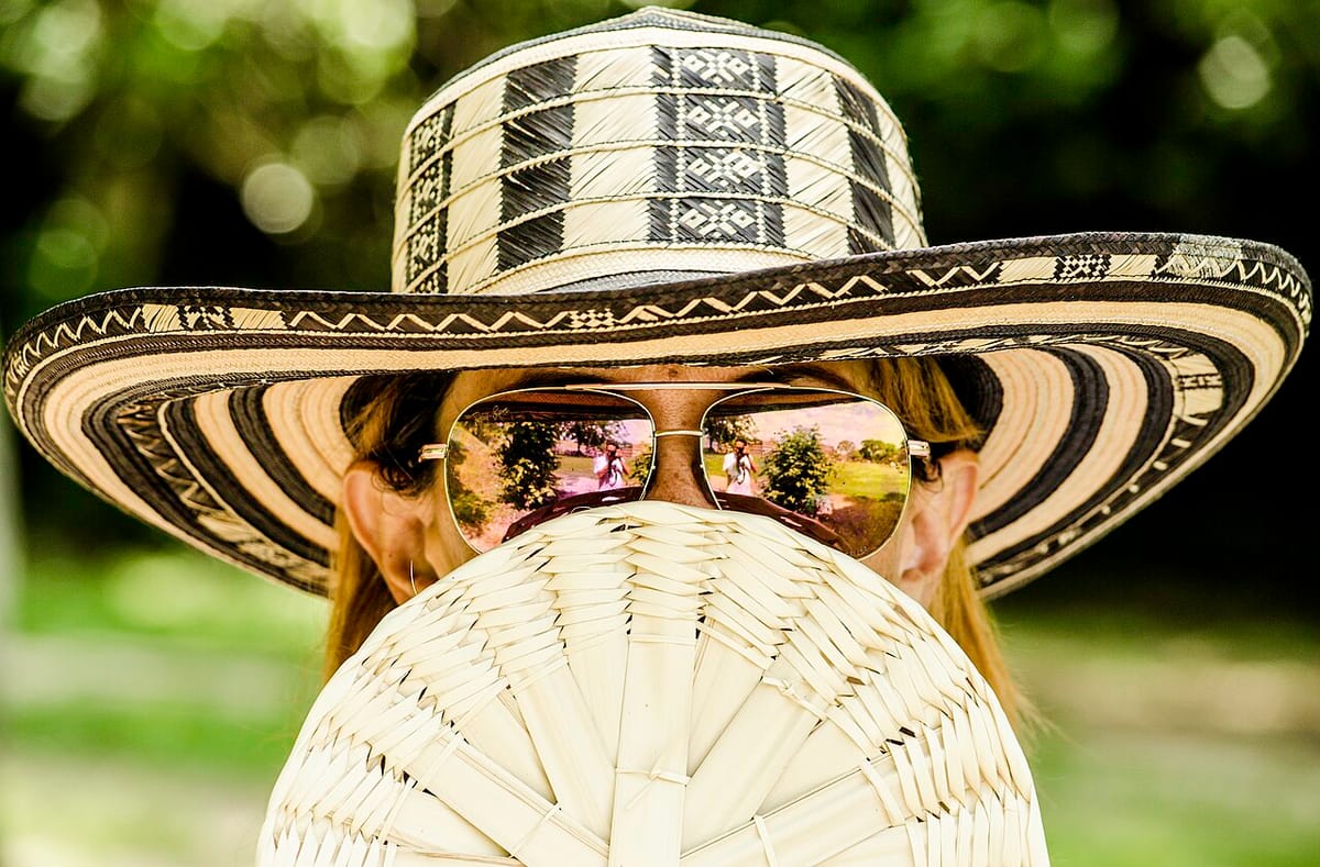 Mujer con sombrero de paja y gafas de sol tapándose la cara con un abanico