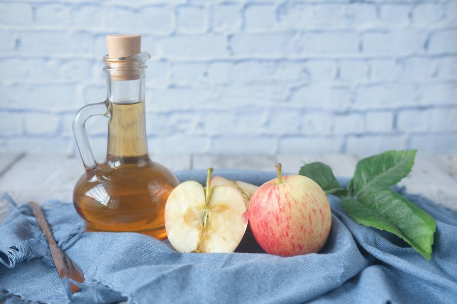 Botella de vinagre de manzana junto a una manzana fresca